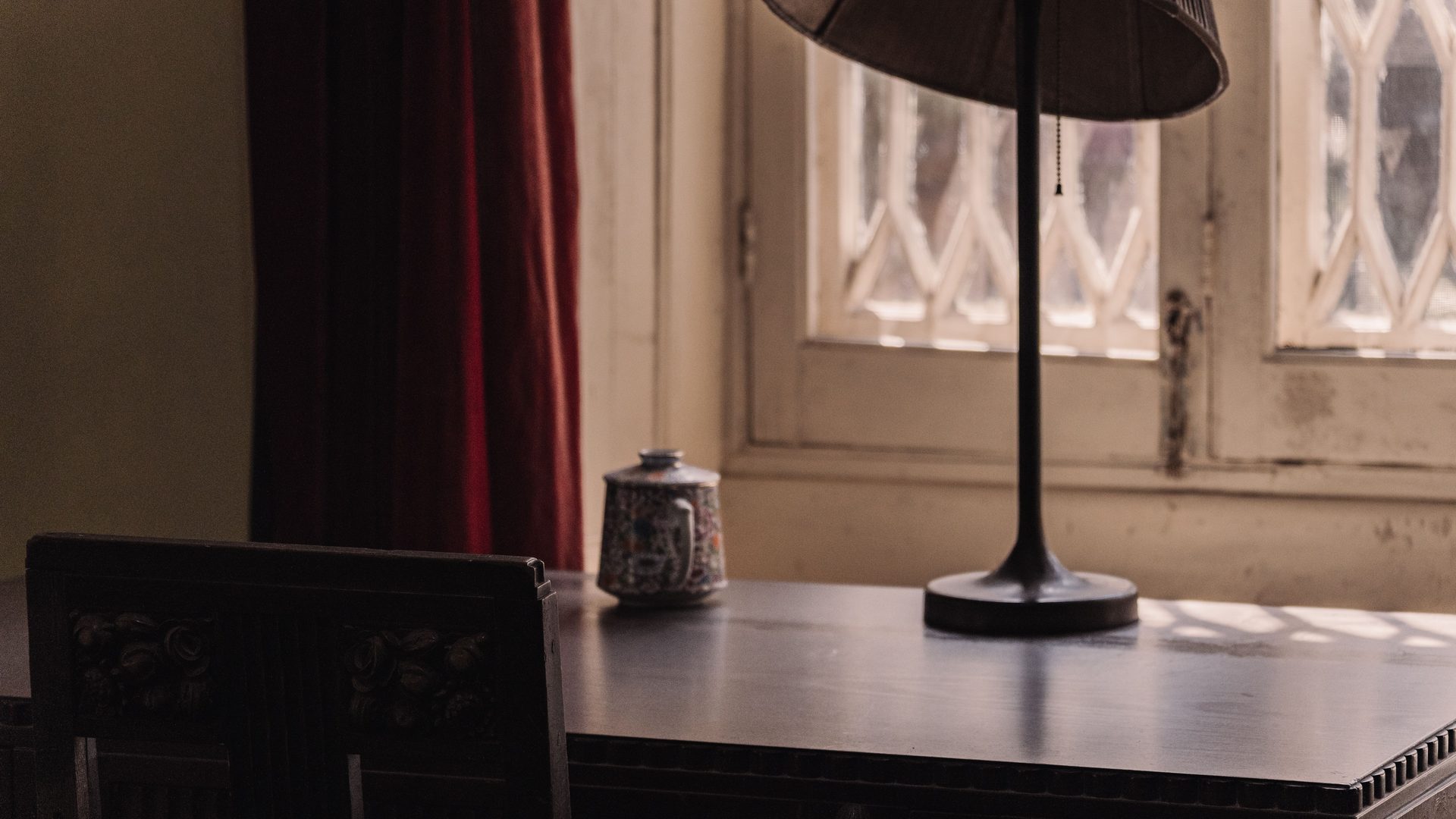 A table lamp and a small ceramic jar on a dark table beside a lattice window