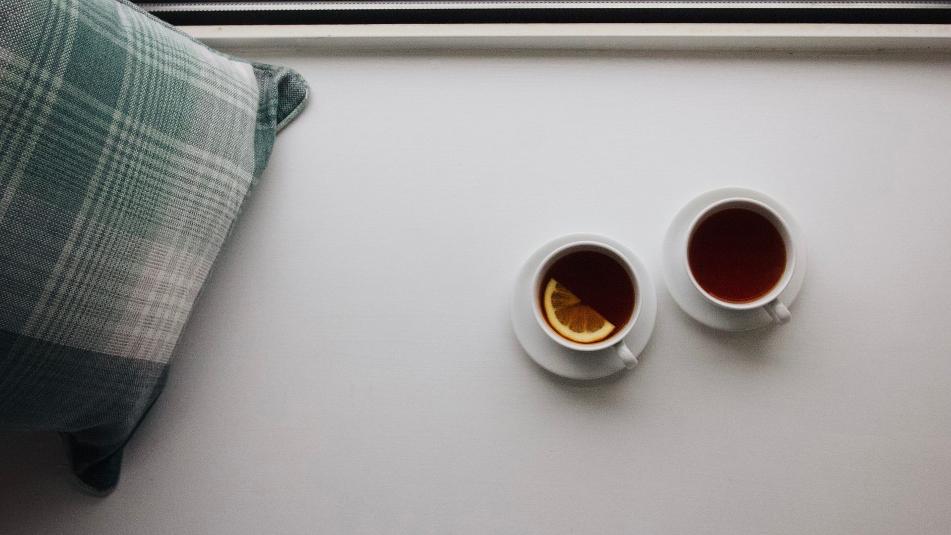 Two cups of tea side by side on a pale table, seen from above