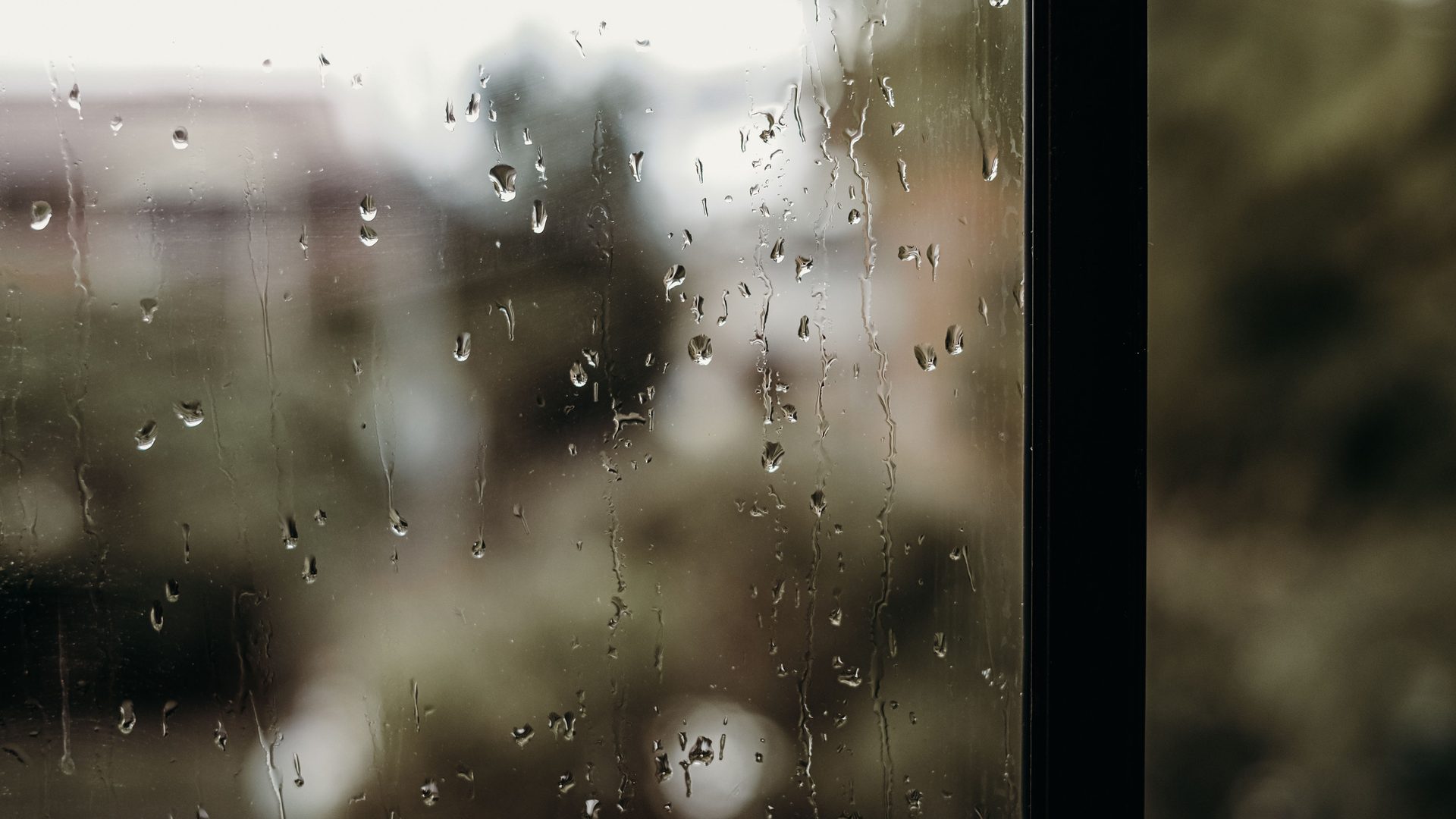 Rain running down a window pane, the view beyond it blurred