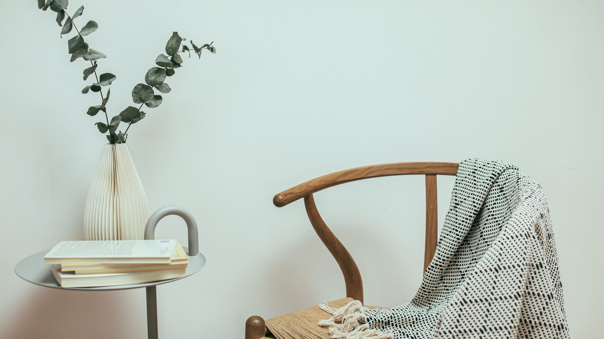 A vase, a wooden chair and a folded throw against a pale wall