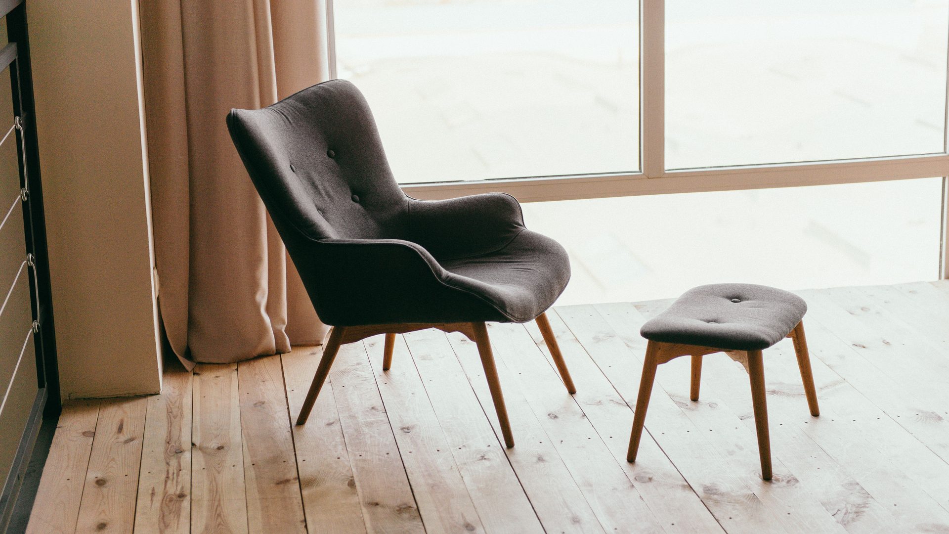 An armchair and footstool beside a curtained window
